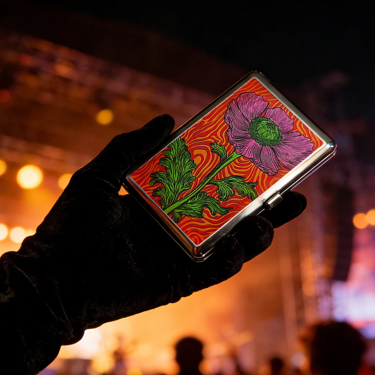 A hand holds a vintage metal card and cash case with an art deco design featuring pink and green floral patterns against a da