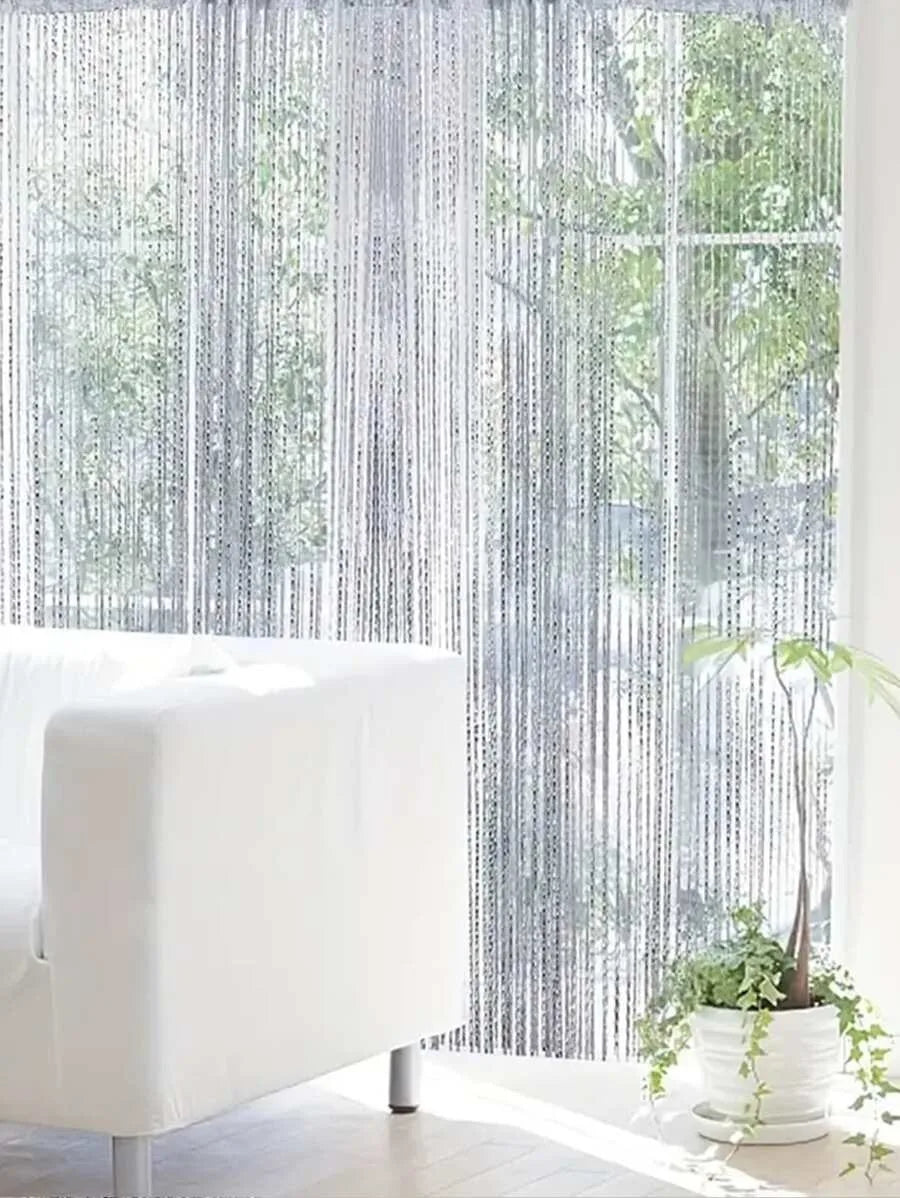 Ein weißes Sofa vor einem Fenster, das mit einem durchscheinenden, vertikalen Perlen-Strangvorhang bedeckt ist.