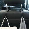 A pair of universal car headrest hooks with storage hangers are shown in a black car interior.