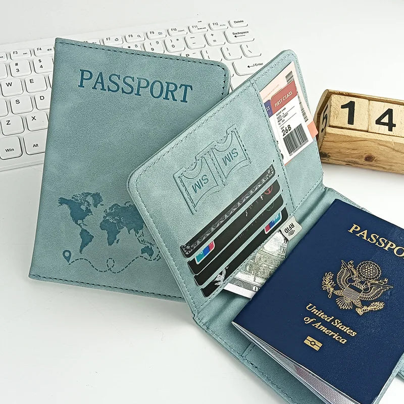 A teal leather passport holder with card slots is shown next to a laptop and wooden blocks.