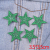 A set of five green glitter star iron-on embroidered patches sewn onto a light blue denim fabric.