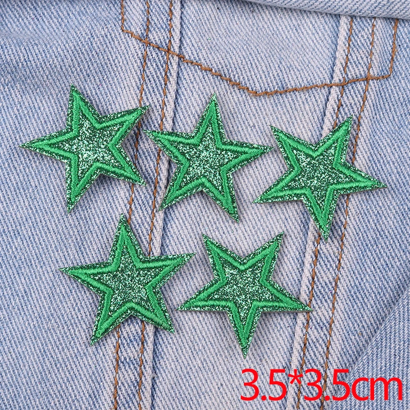 A set of five green glitter star iron-on embroidered patches sewn onto a light blue denim fabric.