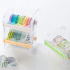 A clear plastic storage box holds various colored washi tapes and a cutter.