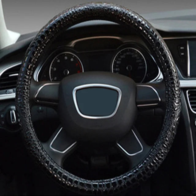 Close-up view of a black crocodile grain leather car steering wheel cover inside a vehicle