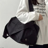 A person is holding a large black canvas travel tote bag with a strap against a white shirt.