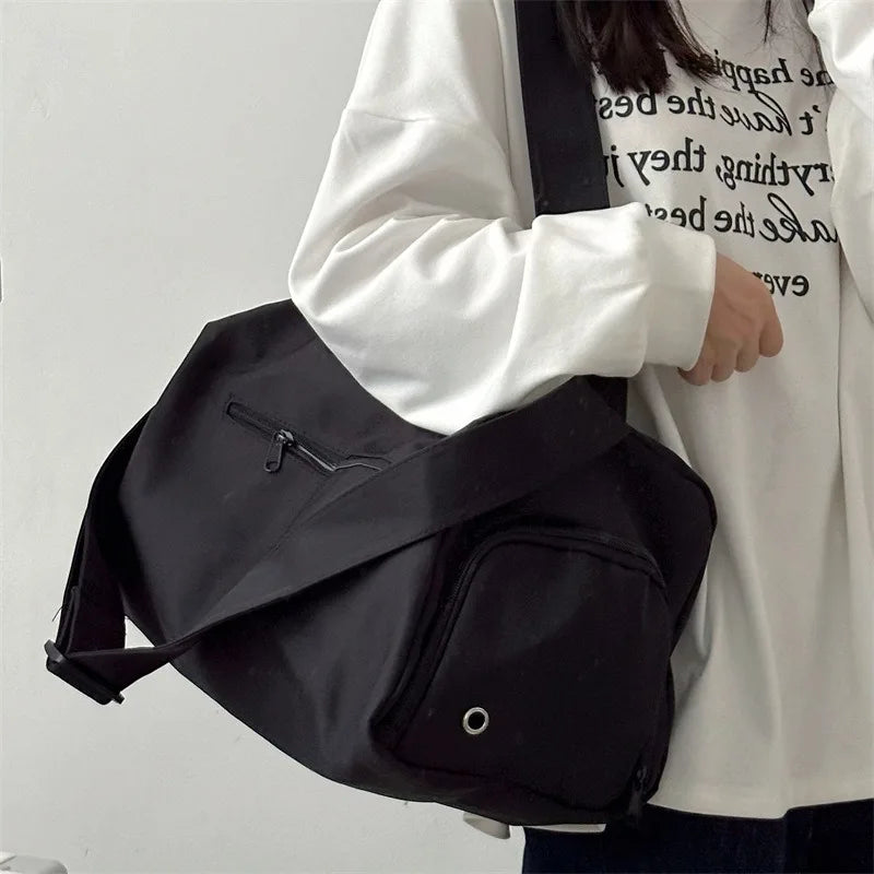 A person is holding a large black canvas travel tote bag with a strap against a white shirt.