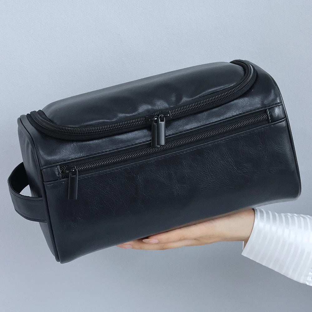 A black leather toiletry bag with a zipper is held in a person's hand against a light gray background.