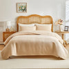 A beige plaid queen bedspread set with matching pillow shams displayed on a light wood bed frame.