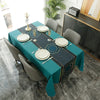 A long dining table set for a meal with a teal tablecloth, white plates, and gray chairs in a modern setting.