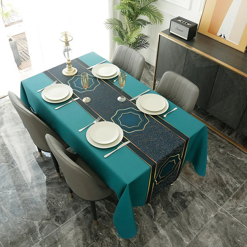 A long dining table set for a meal with a teal tablecloth, white plates, and gray chairs in a modern setting.