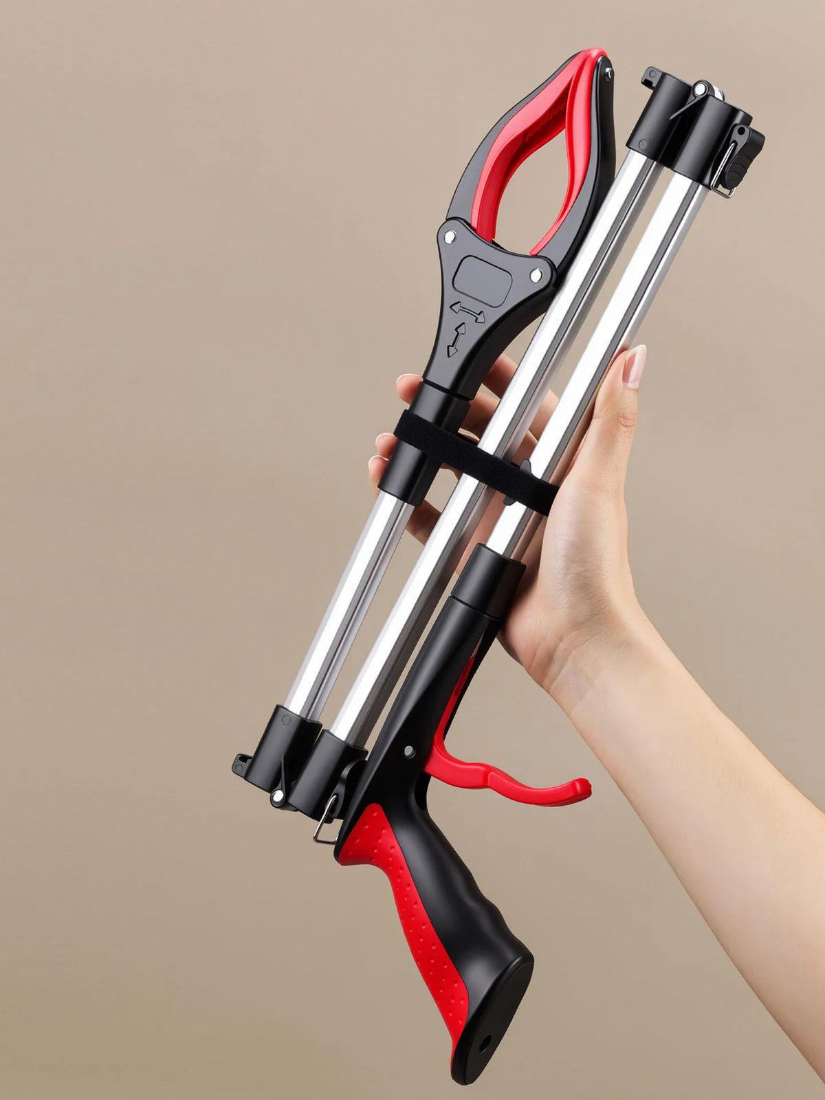 A hand holds a red and black foldable grabber tool with silver arms, demonstrating its use for cleanup.