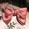 A satin pink silk bow hair clip with a ponytail holder displayed on a white surface.