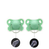 A pair of light green silicone baby pacifiers with a flower design and protective cover shown next to the anatomical shape of