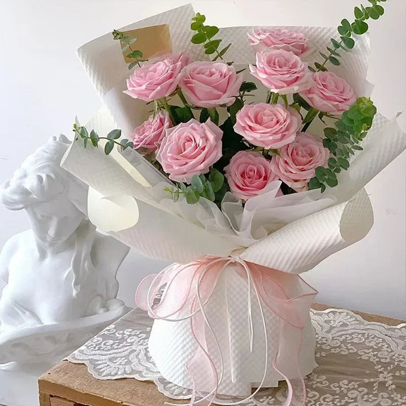 Pink roses in white paper wrapping tied with a pink organza ribbon for DIY crafts and gifts