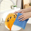 A hand is wiping an orange-colored citrus fruit with a blue microfiber cleaning cloth in a kitchen sink.