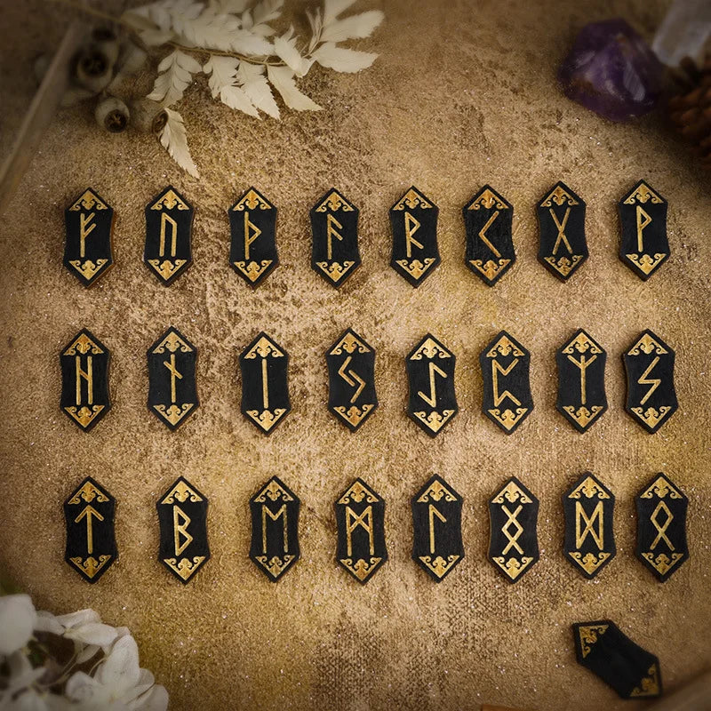 A collection of wooden rune stones arranged on a textured surface with some dried foliage and a purple stone.