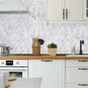 A kitchen countertop featuring a white marble backsplash and light wood countertop with white cabinetry.