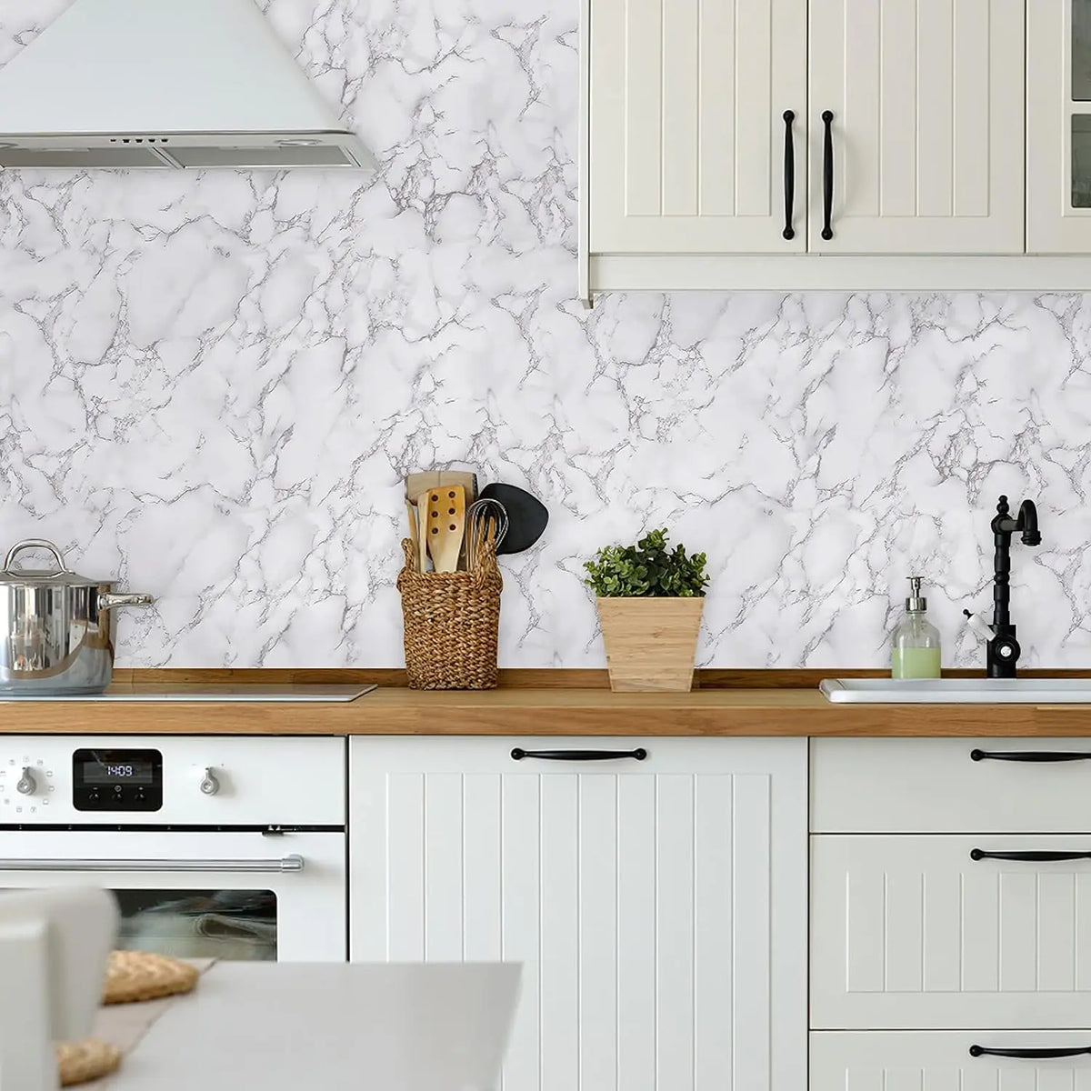 A kitchen countertop featuring a white marble backsplash and light wood countertop with white cabinetry.