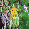 A yellow fruit fly trap kit with a glass jar and pheromone lure hanging from a branch.