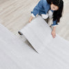 A young woman is carefully peeling a roll of white wood grain peel and stick wall decals.