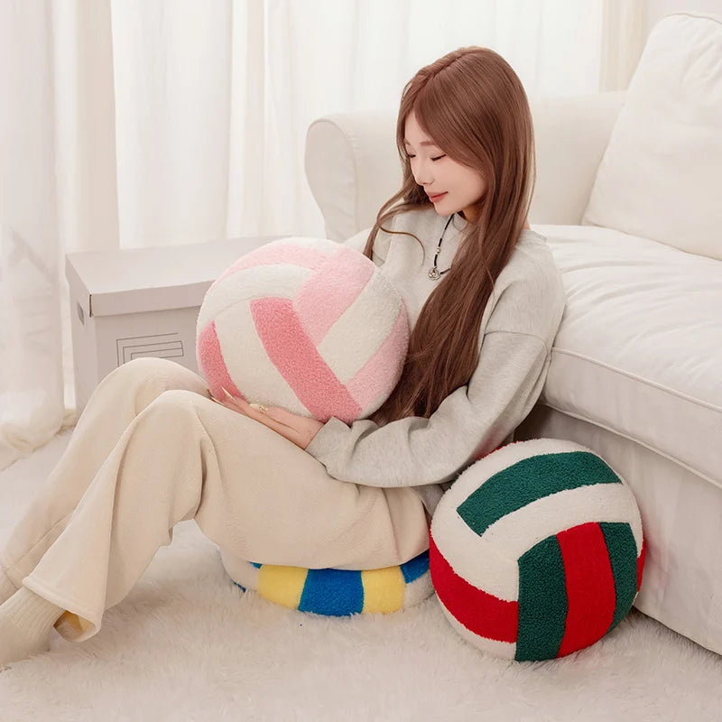 A woman is sitting on a white sofa holding a pink and white simulation volleyball plush toy pillow.
