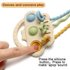 A hand holds a beige silicone bear teether with various colored textured parts and a pull string.