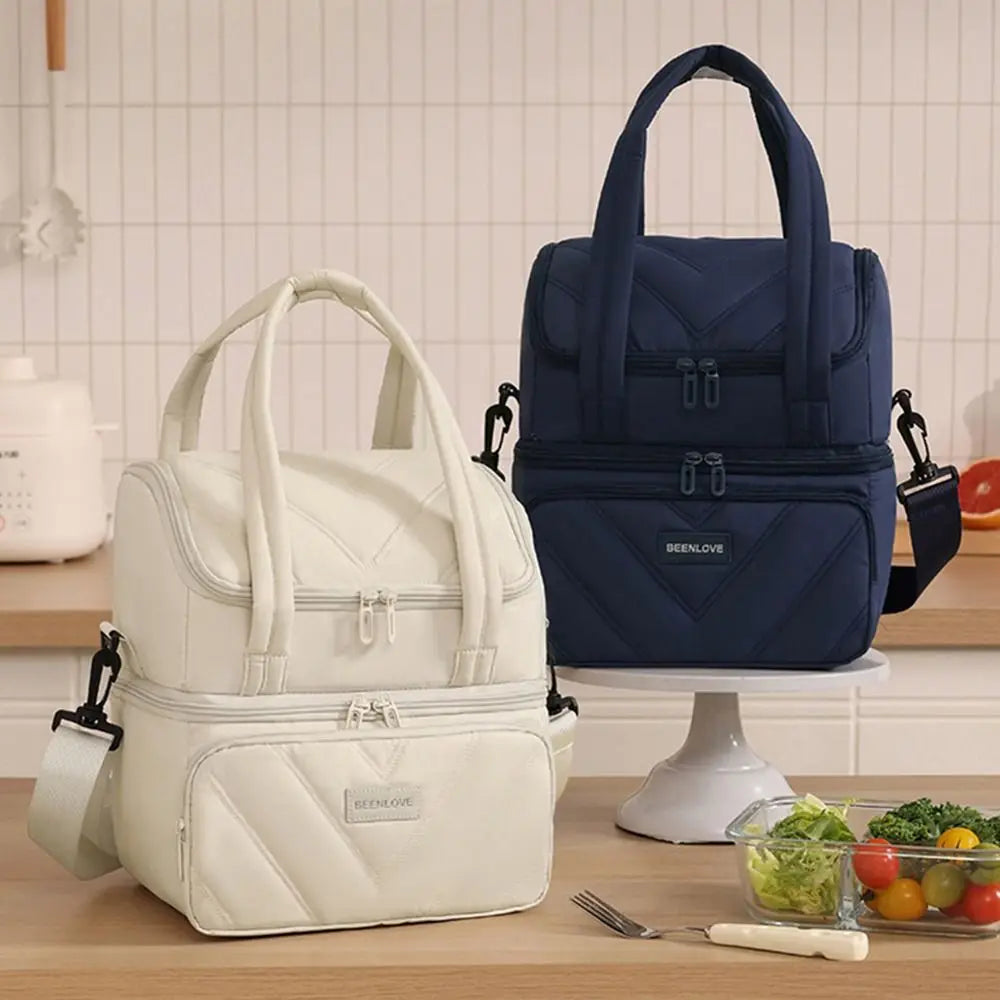 A white insulated lunch bag is shown next to a navy blue one on a wooden table.