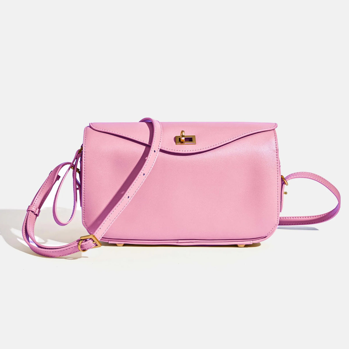 A pink genuine leather square crossbody bag with a gold lock and purple strap.