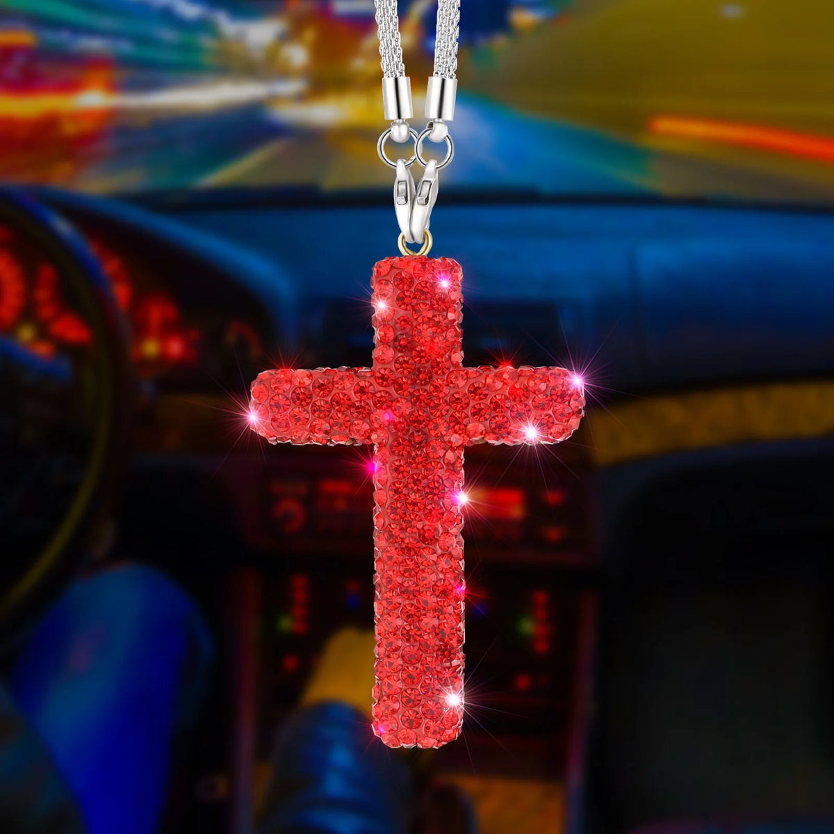 A red rhinestone cross pendant suspended by a silver chain, displayed in a car interior setting.