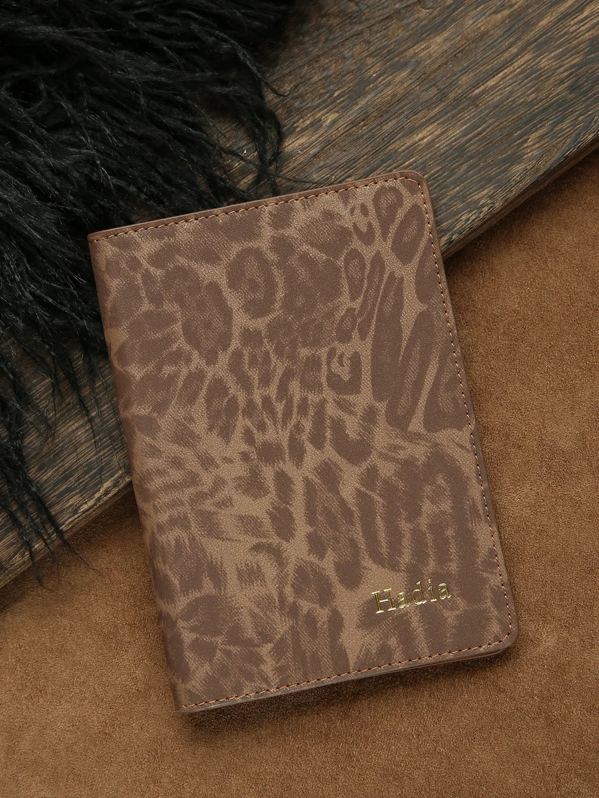 A brown leopard print passport holder with gold name embossing resting on a tan surface.