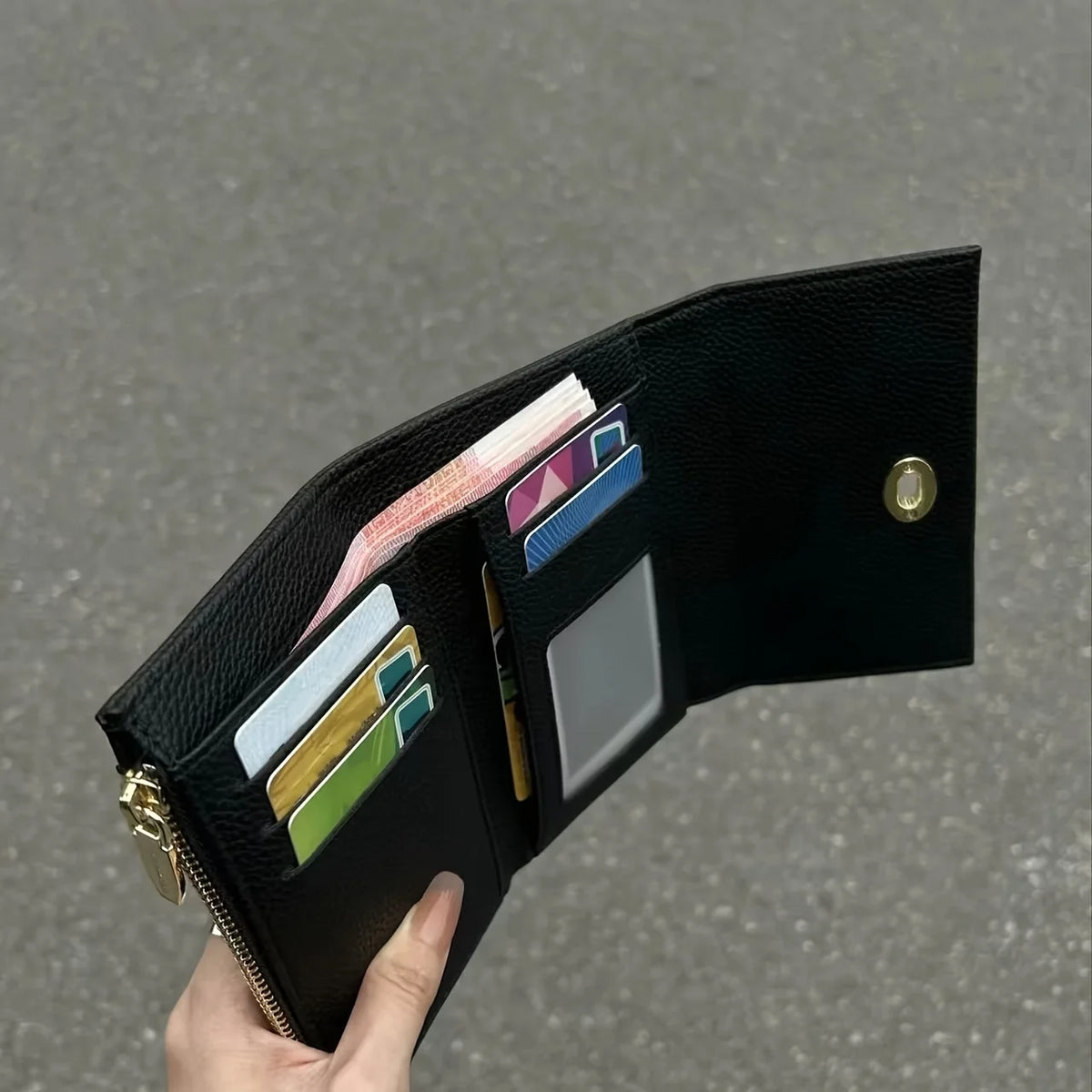 A hand holds a sleek black compact wallet displaying various cards and cash inside.