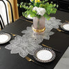 A black table set featuring ornate white lace placemats, gold cutlery, and a vase of yellow and white flowers.