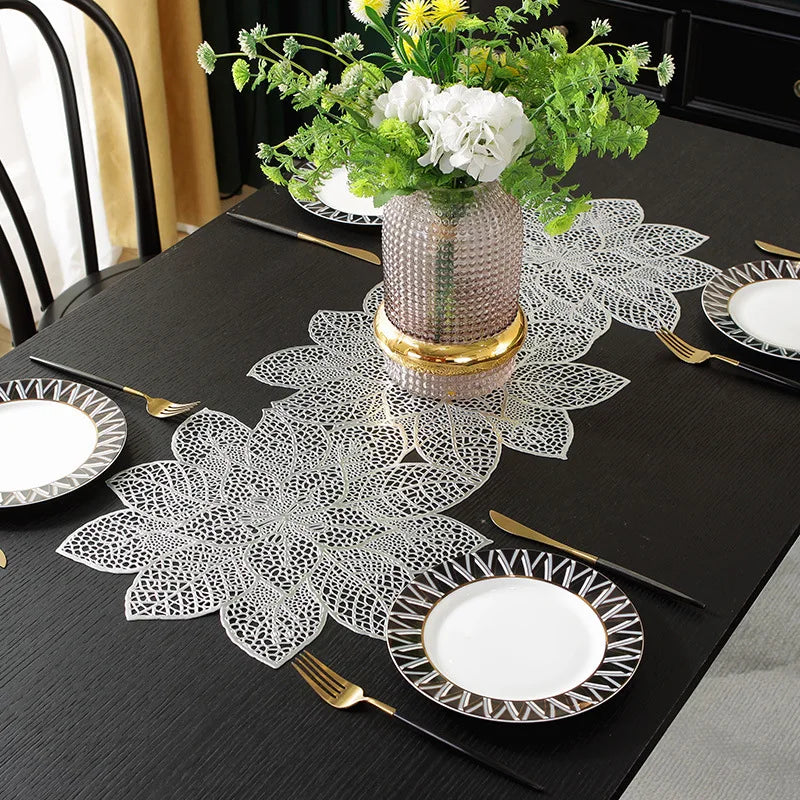 A black table set featuring ornate white lace placemats, gold cutlery, and a vase of yellow and white flowers.