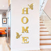 Gold acrylic wall stickers shaped like the letters H O M E, featuring butterfly designs, displayed on a white wall.