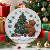 A Christmas embroidery kit featuring a handcrafted set with a green pine tree, a brown bear, and festive ornaments.