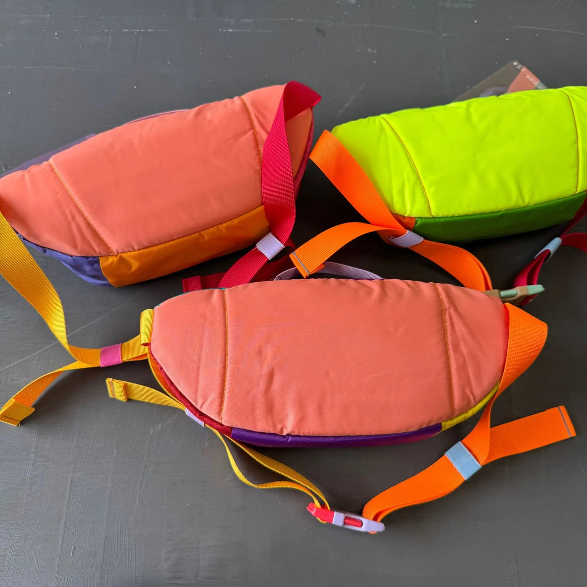 A collection of color block waterproof nylon fanny packs in orange, pink, and lime green.