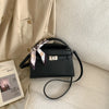 Schwarze elegante PU-Leder-Clutchtasche mit rosa-weiß gestreifter Schleifenverzierung auf cremefarbigem Stoff.