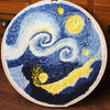 A circular cross stitch embroidery featuring a night sky with swirling blue and yellow stars and a dark silhouette of a mount