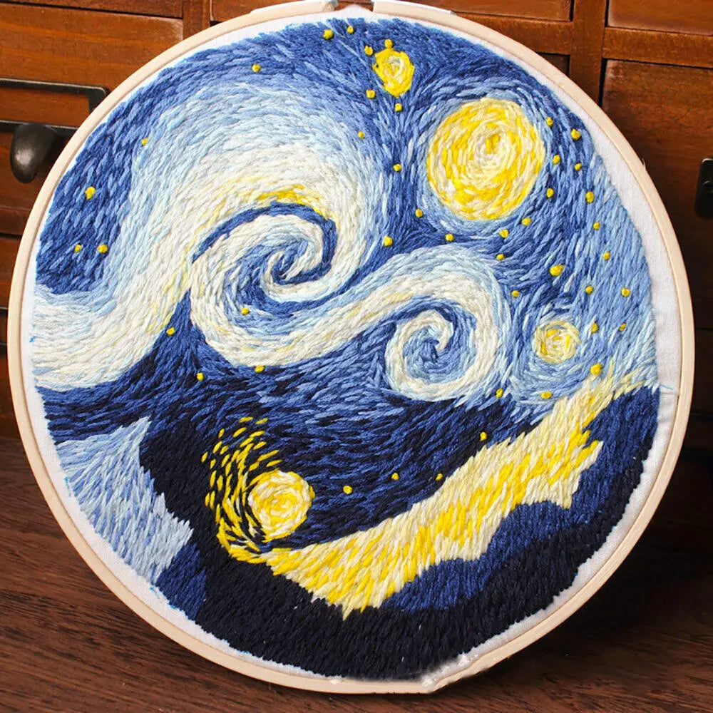 A circular cross stitch embroidery featuring a night sky with swirling blue and yellow stars and a dark silhouette of a mount