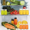 A refrigerator shelf displaying various green and orange juice bottles and fresh vegetables.