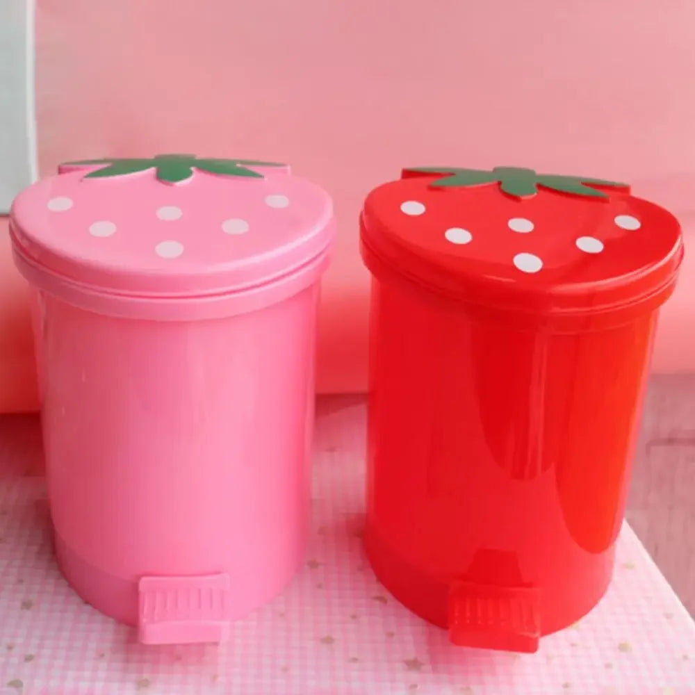 Pink and red mini strawberry trash cans with pop-up lids sitting on a pink surface.