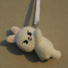 A white, fluffy cat-like plush doll with pink ears is hanging by a white strap against a beige background.