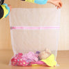 A clear mesh laundry bag filled with pink and yellow clothing, being held by a person's hand.