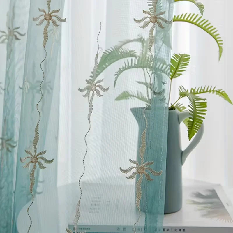 A sheer teal curtain decorated with delicate floral embroidery, featuring a green fern plant in a vase.