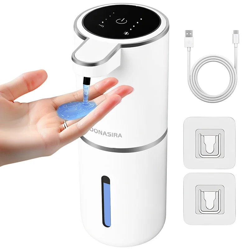 A white touchless automatic soap dispenser is shown being used by a hand, with charging cables and replacement parts displaye