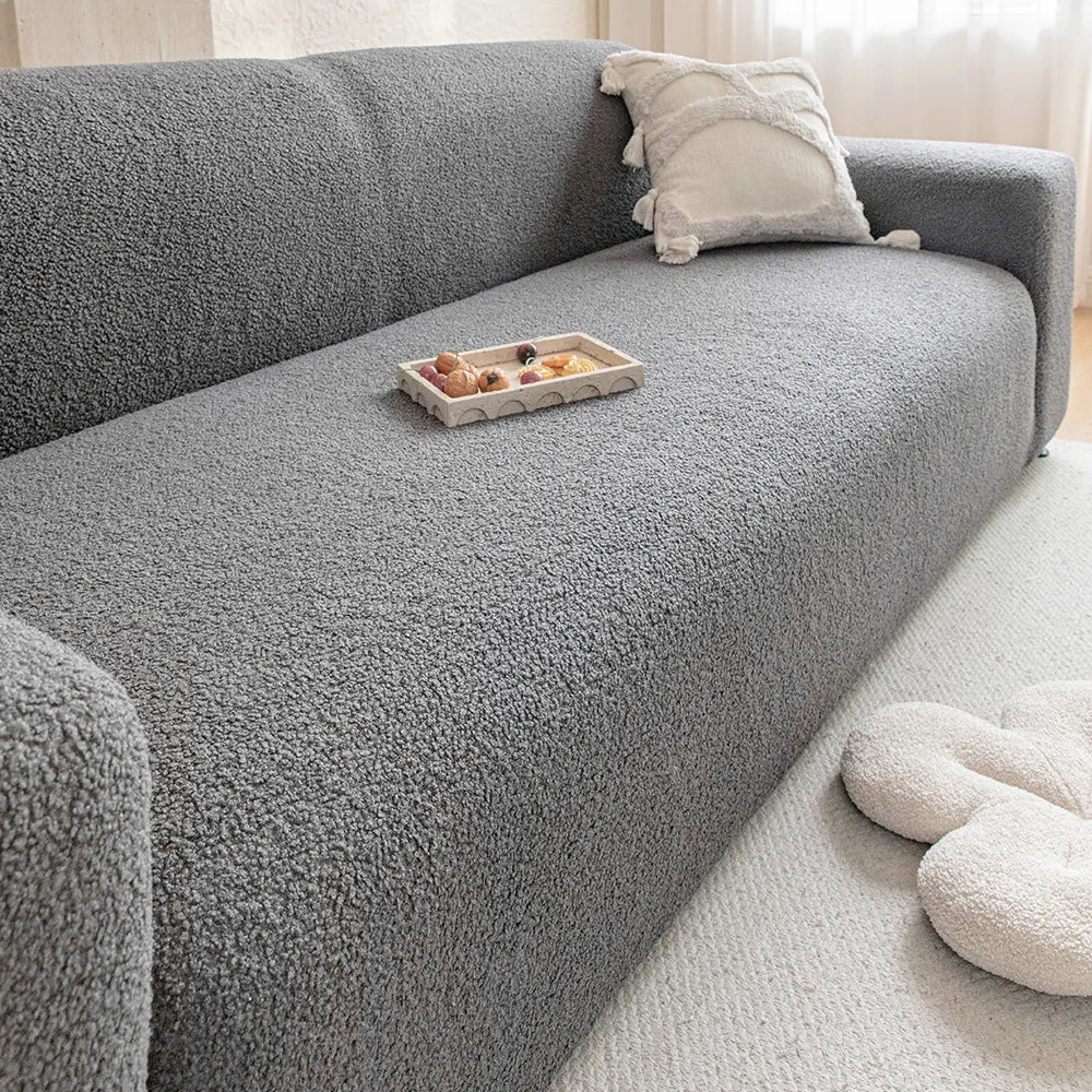 A gray plush sofa cover with a light beige throw pillow and a small wooden dish on the surface.