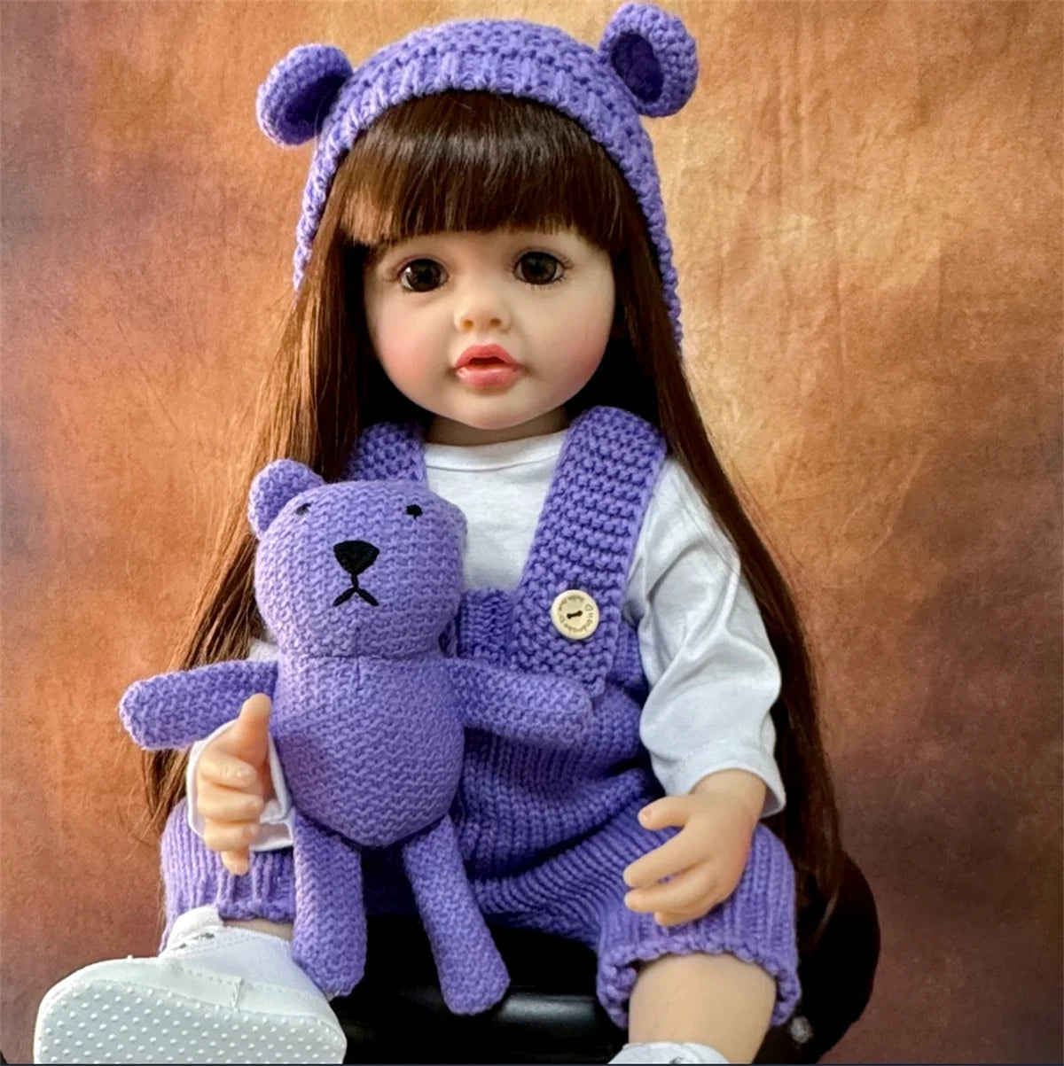 A purple knitted baby doll wearing a matching hat and vest, with long brown hair.