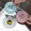 A hand is placing a pink silicone sink drain filter strainer onto a stainless steel sink drain.
