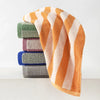 A stack of soft plaid cotton bath towels in shades of orange, green, purple, and blue.