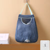 A dark blue mesh garbage bag holder is hanging on a wall, featuring a fabric pouch and hooks.